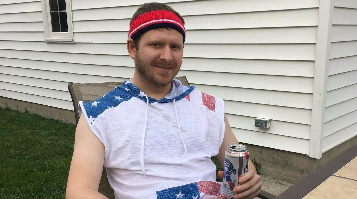 Sam sits in a patio chair wearing a holiday shirt and holding an unlabeled can.