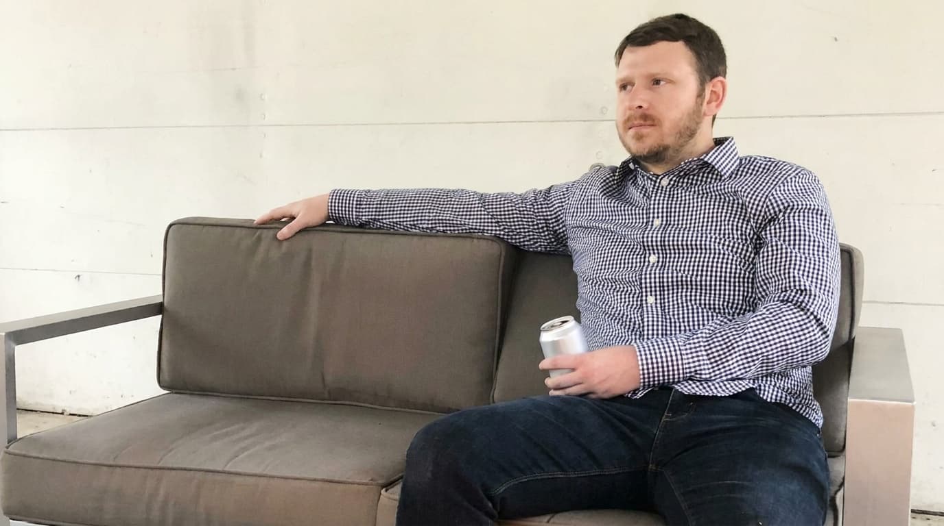 Sam sits on a couch holding a plain can while the room remains quiet.