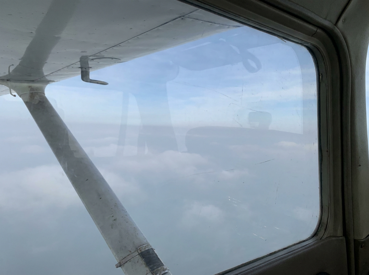 Soft clouds and pale sky from a cockpit window.